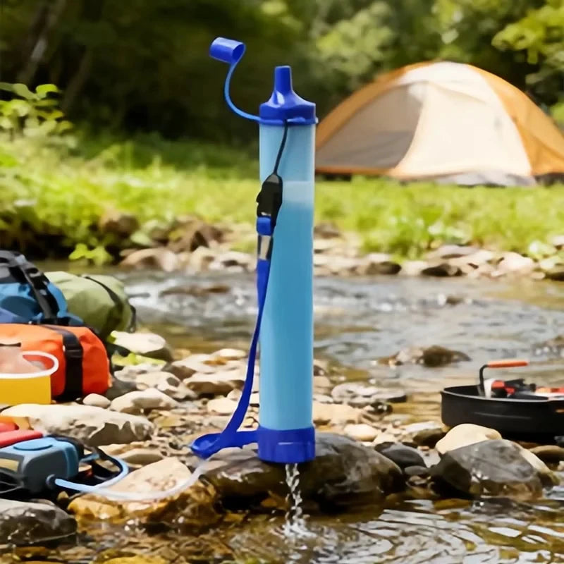 Blue Portable Water Filter Straw on a rocky stream with camping gear and a tent in the background.