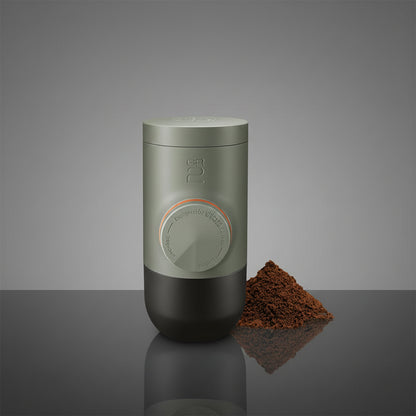 Green portable coffee maker with ground coffee on a white background