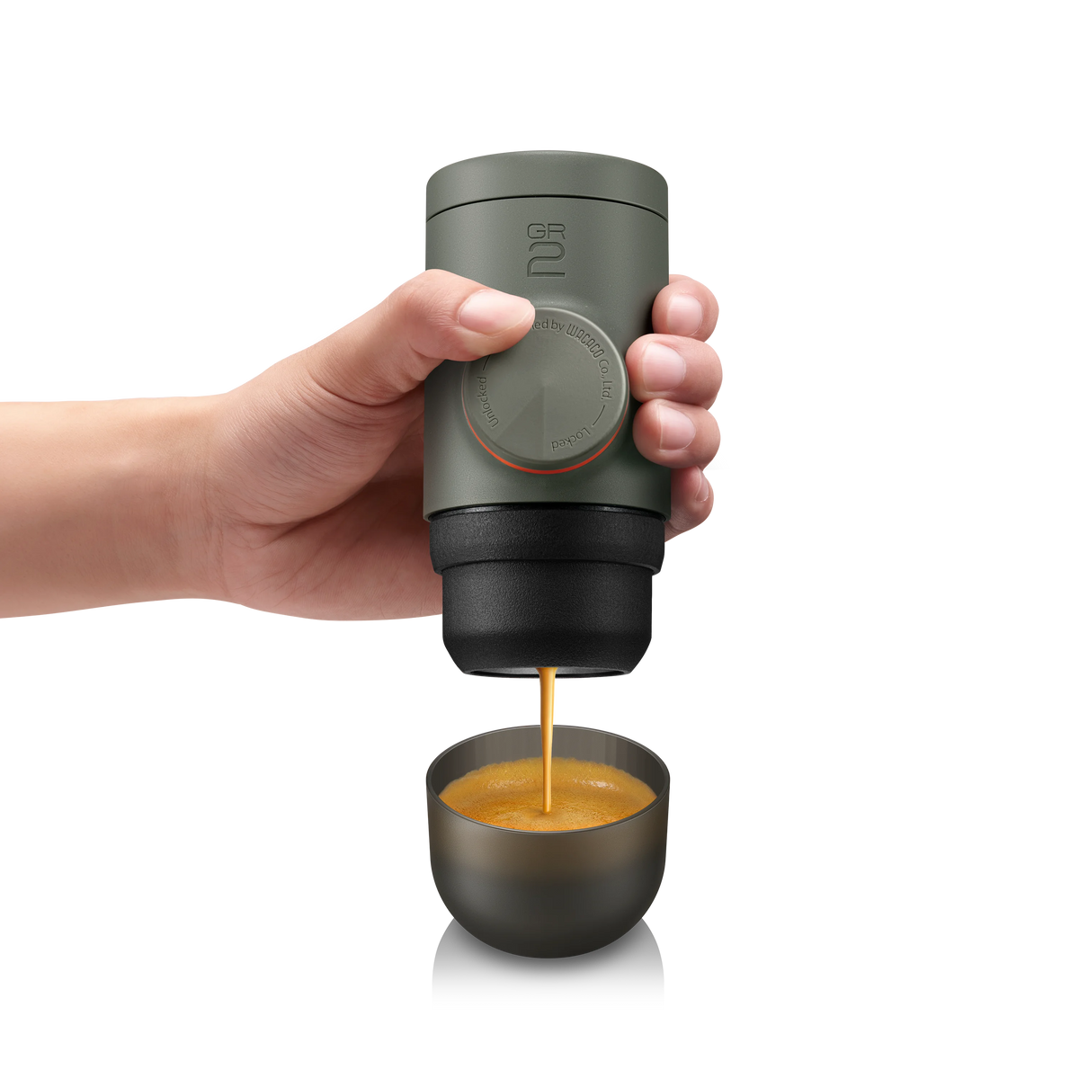 Hand holding a portable coffee maker dispensing coffee into a small cup on a white background