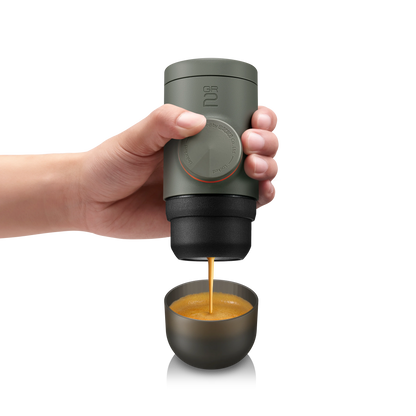 Hand holding a portable coffee maker dispensing coffee into a small cup on a white background