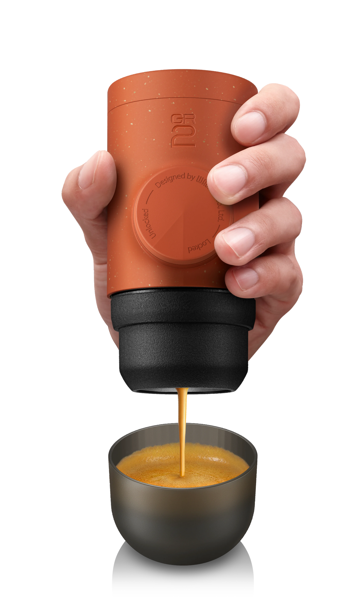 Hand holding a terracotta-colored portable coffee maker dispensing coffee into a small cup.