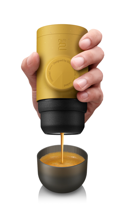 Hand holding a yellow portable coffee maker pouring coffee into a small cup on a transparent background