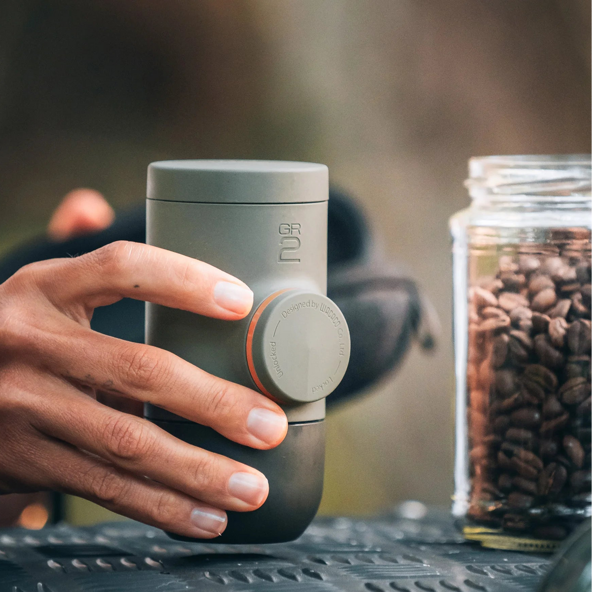 Hand holding a Portable Espresso Maker with coffee beans and a jar in the background